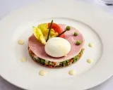Une assiette blanche présente une délicieuse macédoine de légumes, garnie de jambon, d'un œuf mollet, de tomates et de laitue.