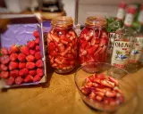 Bocaux de fraises coupées prêtes pour un rhum arrangé fraise menthe. Bouteilles de rhum à proximité.