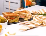 Un délicieux club sandwich, garni de tomates et de laitue, servi avec des cornichons et des chips.