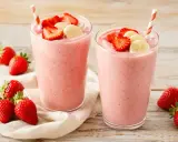 Deux verres de smoothie fraise banane, garnis de fruits frais. Parfait pour une pause gourmande et rafraîchissante.