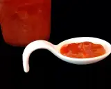 Une cuillère blanche présente une délicieuse confiture fraise rhubarbe, avec un pot en arrière-plan.