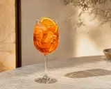 Une composition Aperol Spritz rafraîchissante, avec des glaçons et une tranche d'orange, sur une table en marbre baignée de soleil.