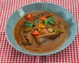Langue de bœuf en sauce piquante, garnie de cornichons, tomates cerises et persil, servie dans un bol bleu sur une nappe à carreaux rouges et blancs.