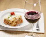 Un verre de vin rouge pétillant à côté d'une portion de lasagnes appétissante. La question se pose : quel vin avec des lasagnes pour un accord parfait ?