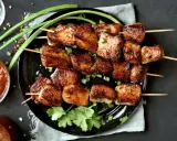Brochettes de porc mariné, grillées à la perfection, garnies d'oignons verts et de coriandre fraîche. Accompagnées d'une sauce épicée.