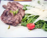 Délicieuse tagliata de boeuf grillée, servie avec une salade verte, copeaux de parmesan et une moitié de tomate cerise.