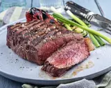 Un savoureux rumsteck de boeuf grillé, coupé en tranches, servi avec des légumes rôtis et des oignons verts sur une assiette grise.