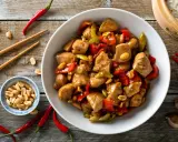 Un délicieux poulet kung pao, garni de cacahuètes croquantes, de poivrons rouges et verts, prêt à être dégusté avec des baguettes.