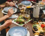 Un verre de vin blanc beurré, des toasts à l'avocat et un plateau de fromages et fruits sur une table dressée pour un dîner convivial.