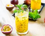 Un verre de cocktail fruit de la passion, garni de menthe fraîche, entouré de fruits entiers et coupés.