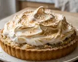 Une délicieuse tarte noix de coco avec une meringue dorée et aérienne, parsemée de copeaux de noix de coco grillés.