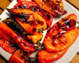 Poivrons rouges et orangés grillés au barbecue, légèrement noircis par la flamme, sur une assiette blanche. Un délice estival.