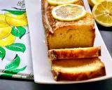 Gâteau moelleux au citron, glacé et garni de rondelles de citron. Ce délice, un gâteau huile d'olive, est servi sur une assiette blanche avec un torchon orné de citrons.