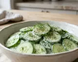 Salade fraîche de concombre à la crème, garnie d'aneth et de poivre noir. Un délice simple et rafraîchissant.