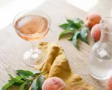 Un verre de vin de pêche rosé, des pêches fraîches et une carafe d'eau glacée sur une table en bois.