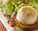 Une délicieuse salade de chèvre chaud sur toast, garnie de lardons et de persil frais, sur une assiette blanche.