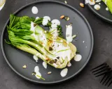 Une assiette de pak choi cru arrosé d'une sauce crémeuse, garni de graines et de zeste de citron vert.
