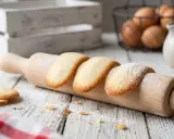 Des biscuits langue de chat dorés, saupoudrés de sucre glace, reposent sur un rouleau à pâtisserie en bois.