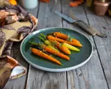 Carottes glacées au miel, colorées et appétissantes, garnissent une assiette sur une table en bois rustique. Une serviette à motifs floraux complète la scène.