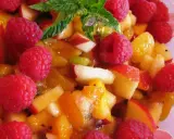 Une délicieuse salade de fruits d'été, pleine de framboises, pêches et abricots juteux, garnie de menthe fraîche.