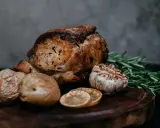 Un délicieux roti de veau au four, accompagné de pommes de terre rôties, d'ail confit, de rondelles de citron et de romarin frais sur une planche en bois.