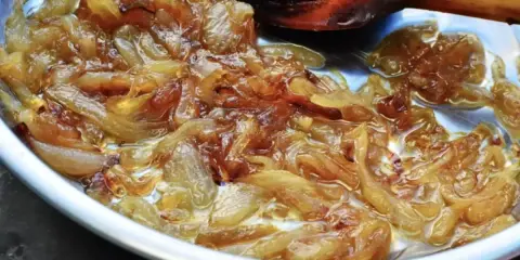 Oignons nouveaux caramélisés dans une poêle, prêts pour une délicieuse recette. La cuisson lente révèle leur douceur.