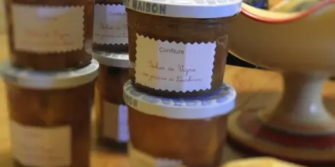 Plusieurs pots de confiture maison, dont une délicieuse confiture de pêches de vignes, sont alignés sur une table en bois.