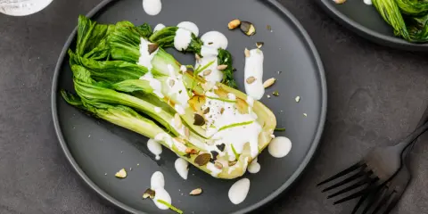Une assiette de pak choi cru arrosé d'une sauce crémeuse, garni de graines et de zeste de citron vert.