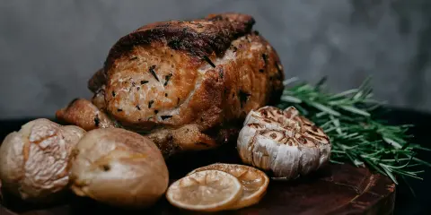 Un délicieux roti de veau au four, accompagné de pommes de terre rôties, d'ail confit, de rondelles de citron et de romarin frais sur une planche en bois.