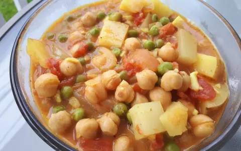 Un savoureux curry de petit pois avec des pois chiches et des morceaux de pommes de terre dans une sauce orangée.