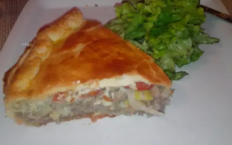 Une part de tourte à la viande grand-mère, dorée et généreuse, servie avec une salade verte croquante. Un délice réconfortant.
