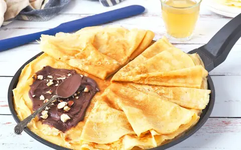 Délicieux crepe a la biere, pliés dans une poêle, garnis de pâte à tartiner au chocolat et noisettes. Une cuillère repose sur le dessus.