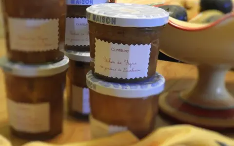 Plusieurs pots de confiture maison, dont une délicieuse confiture de pêches de vignes, sont alignés sur une table en bois.