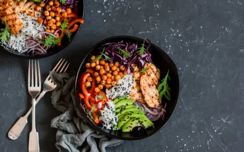 Deux bols de poulet grillé, riz, avocat, pois chiches et chou rouge. Une recette avec salade verte pour un repas sain et coloré.