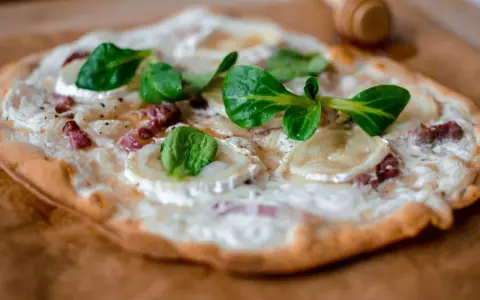 Délicieuse tarte flambée végétarienne garnie de fromage de chèvre, oignons et herbes fraîches.