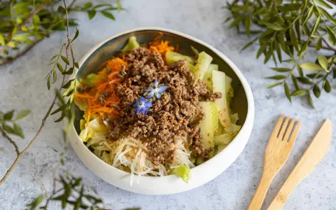 Salade fraîche et colorée avec viande hachée, carottes râpées, concombre et une touche florale. Un plat léger et savoureux.