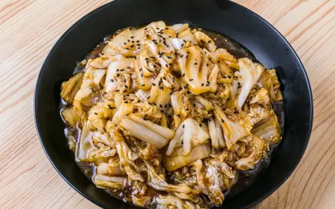 Un plat de recette pak choï sauté, garni de graines de sésame noires et blanches, sur une assiette noire.