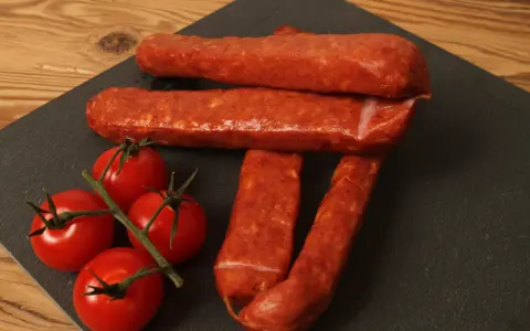 Saucisses sèches et tomates cerises sur une planche d'ardoise, parfait pour une recette de saucisse gendarme.