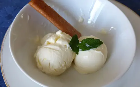 Deux boules de glace au citron onctueuse, garnies de menthe fraîche et d'un biscuit fin, dans un bol blanc.