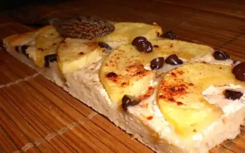Tranche de tarte flambée sucrée aux pommes, cannelle et pépites de chocolat, posée sur un tapis de bambou.