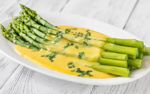 Un bouquet d'asperges vertes nappées d'une sauce hollandaise crémeuse, garnies de persil frais. Une délicieuse idée d'asperges en entrée froide.