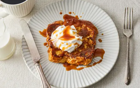 Pain perdu gourmand nappé d'une sauce caramel au miso, garni de crème fouettée. Servi avec une tasse de café et un verre de lait.