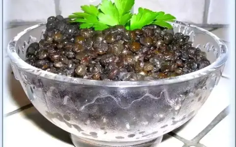 Lentilles beluga, parfaitement cuites, servies dans un bol en verre, garnies de persil frais. Un délice simple et sain.