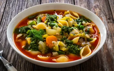 Soupe au pistou recette de chef : un plat coloré de légumes frais, pâtes et pesto, servi dans un bol blanc sur fond de bois.