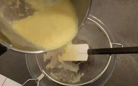 Filtrage de la crème anglaise pour une texture parfaite. Une spatule aide à racler le fond de la casserole.