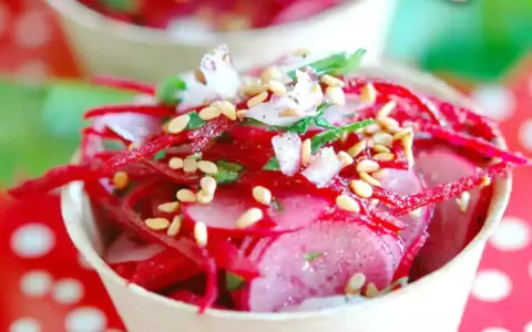Salade de radis rose râpé et en tranches, garnie de graines de sésame et d'herbes fraîches, servie dans un petit pot.