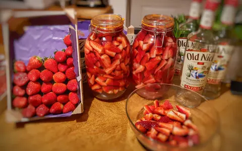 Bocaux de fraises coupées prêtes pour un rhum arrangé fraise menthe. Bouteilles de rhum à proximité.