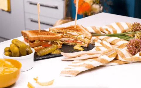 Un délicieux club sandwich, garni de tomates et de laitue, servi avec des cornichons et des chips.
