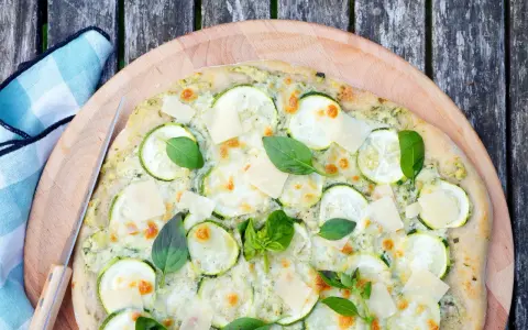 Délicieuse pizza courgette, garnie de fromage fondant, de fines tranches de courgette et de feuilles de basilic frais, prête à être dégustée.