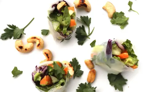 Trois rouleaux de printemps végétariens colorés, remplis de légumes frais et de noix de cajou grillées, parsemés de persil frais.